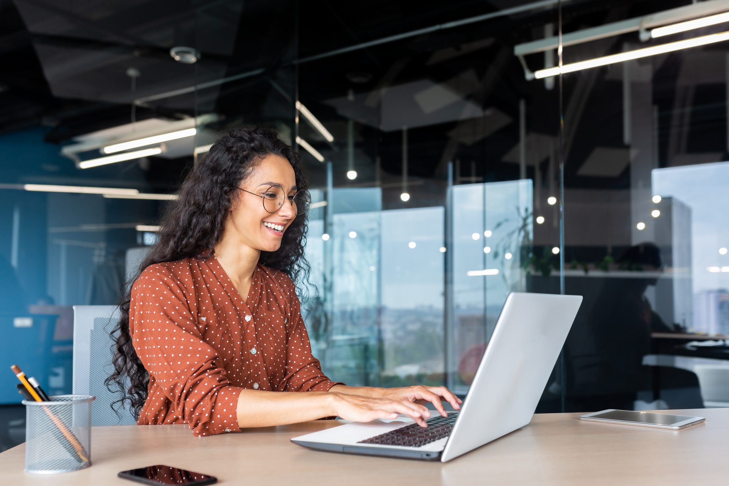 A woman smiles as she works on a laptop.