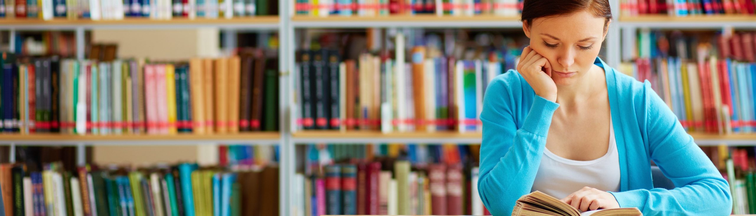 Portrait of clever student with open book reading it in college library